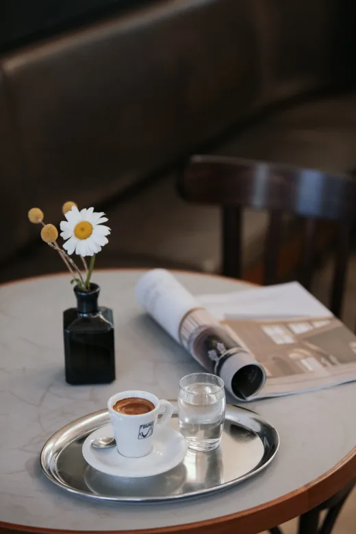 Aufgeschlagene Zeitung, Kaffee und eine Margerite auf dem Tisch