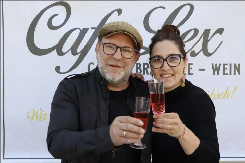 Steffi und Hias Putz-Machater stoßen vor dem Café-Lex-Schriftzug mit Wein an